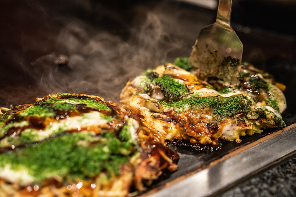 chef use spatula to cut the done okonomiyaki in half on the iron plate, and ready to give the delicious japanese traditional food to the customers