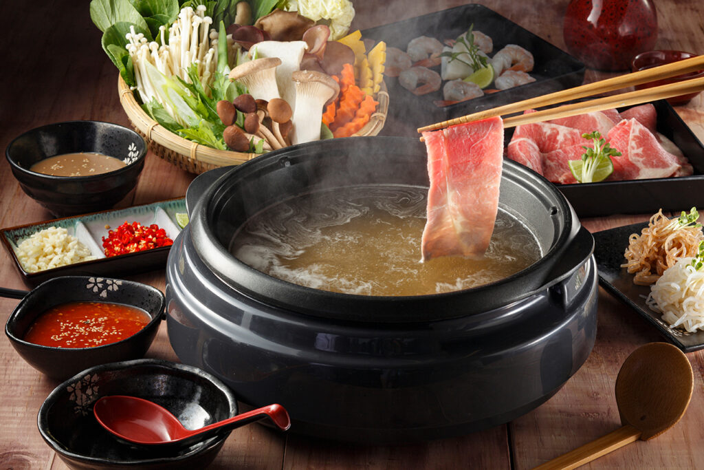 Chopstic holding beef shabu-shabu or sukiyaki. Beef slice on top of hot pot, Fresh beef slices with ingredients background for Japanese shabu-shabu or Sukiyaki.